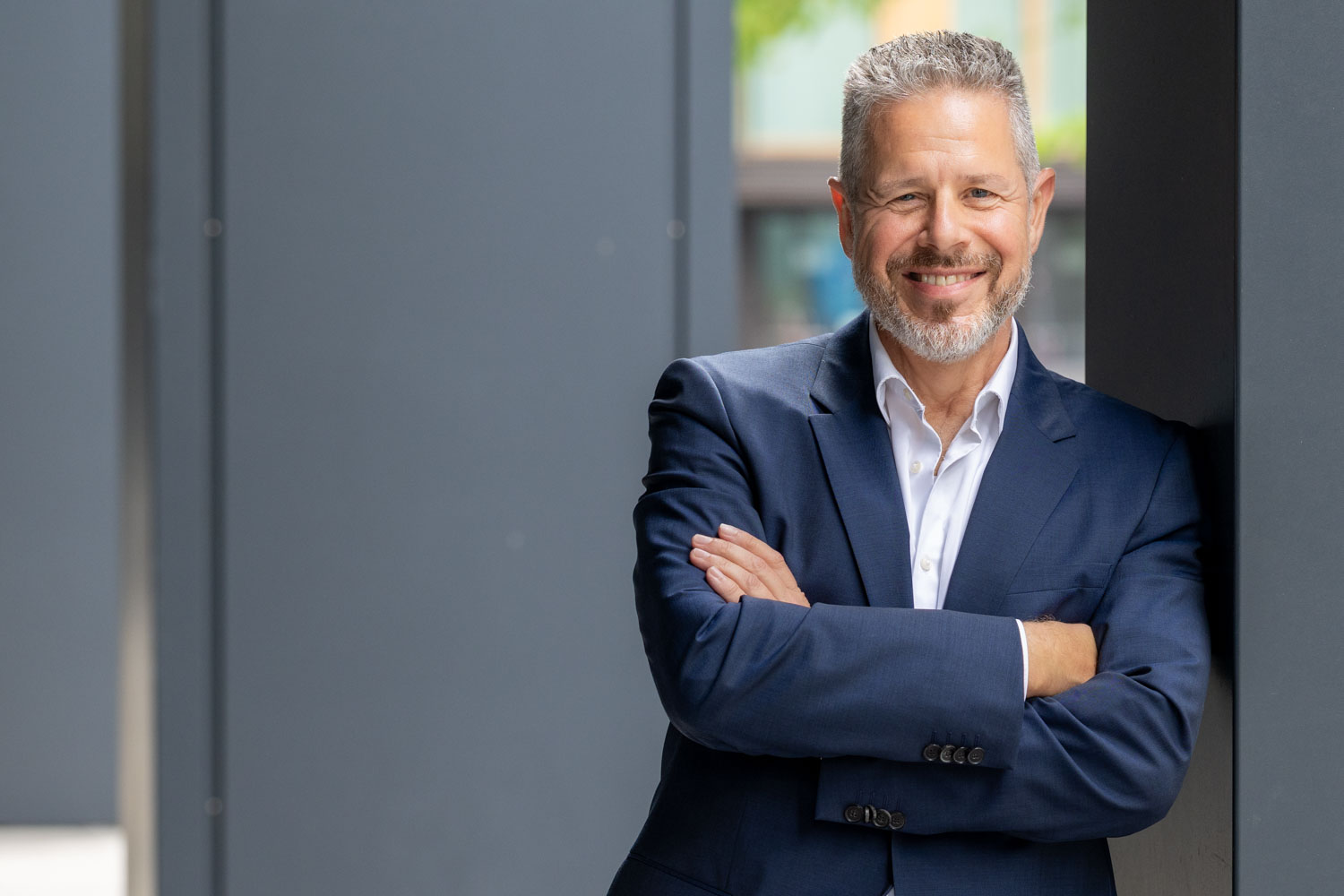 Portrait von Berater und Executive Coach für Führung und Kommunikation Jürgen Pfeiler, der mit verschränkten Armen an einen Pfeiler angelehnt freundlich lächelt.