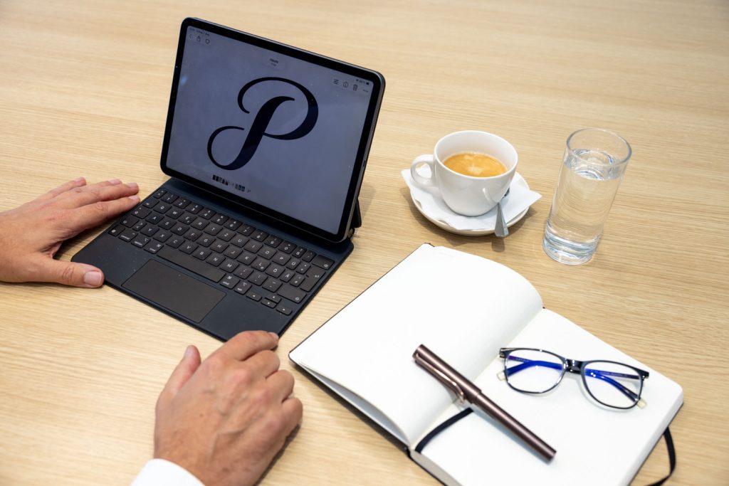 Blick auf Jürgen Pfeilers Notebook in der Vorbereitung auf ein Gespräch über Kommunikation und Führung. Neben dem Notebook ein Notizbuch mit Füllfeder und seiner Brille, ein Kaffee und ein Glas Wasser.